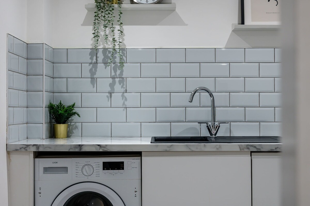 A section of the modern kitchen featuring a black sink with a chrome faucet, light grey subway tile backsplash, and a white washing machine integrated below the marble-effect countertop.