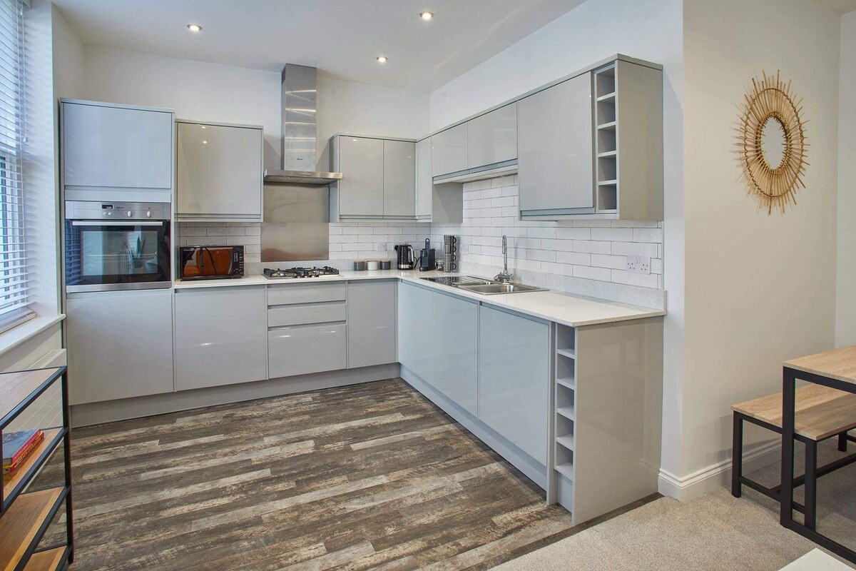 Spacious modern kitchen featuring light grey glossy cabinets, white countertops, a subway tile backsplash, and integrated stainless steel appliances including an oven, microwave, and gas hob.
