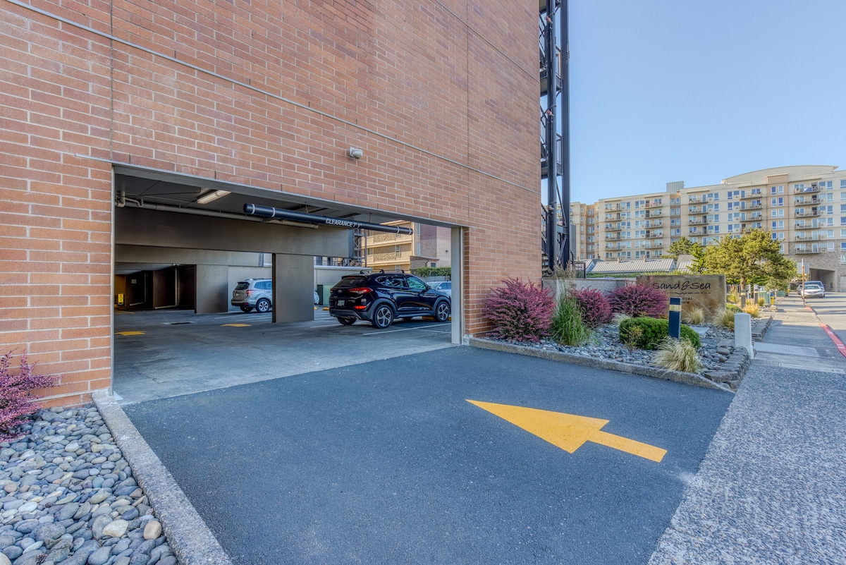 The entrance to an underground parking garage, marked by a yellow arrow on the asphalt, leading into a brick-faced condominium building.