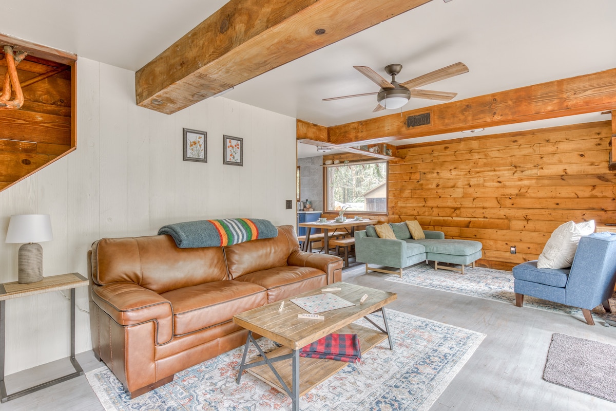 Rustic living room with a brown leather sofa and a light blue sectional, centered around a wooden coffee table on a patterned rug, with exposed wooden beams and a ceiling fan.