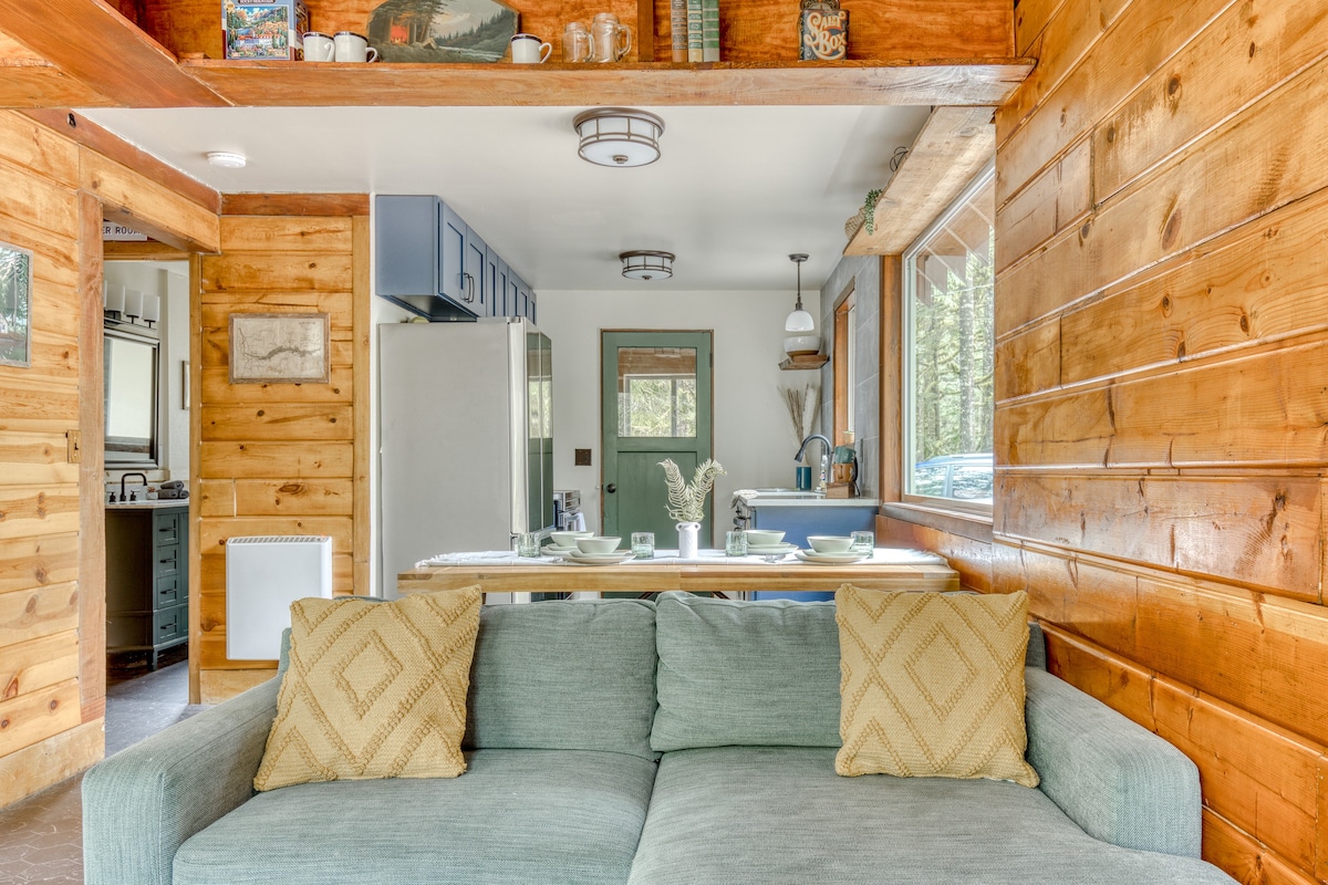 View from the living room into the dining and kitchen area, featuring a light blue sofa, a rustic wooden dining table, and a kitchen with blue cabinetry and a light green door.