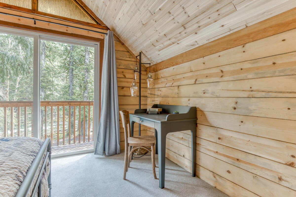 Detail of the bedroom showing a light blue desk with a wooden chair, positioned against a wood-paneled wall. A modern floor lamp with glass shades stands next to the desk, and a sliding glass door leads to an outdoor space.