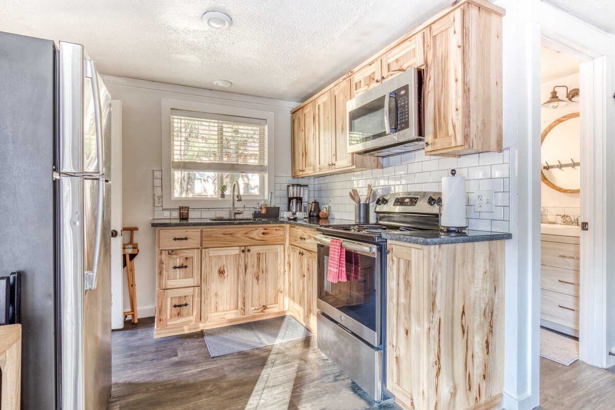 Modern kitchen with light natural wood cabinetry, dark countertops, stainless steel appliances including a microwave and range, and a white subway tile backsplash.