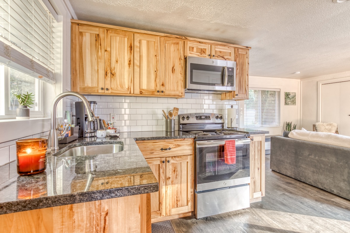 Bright kitchen area with light wood cabinetry, dark granite countertops, a white subway tile backsplash, and stainless steel appliances including a microwave and oven/stove. A window with blinds is above the sink.