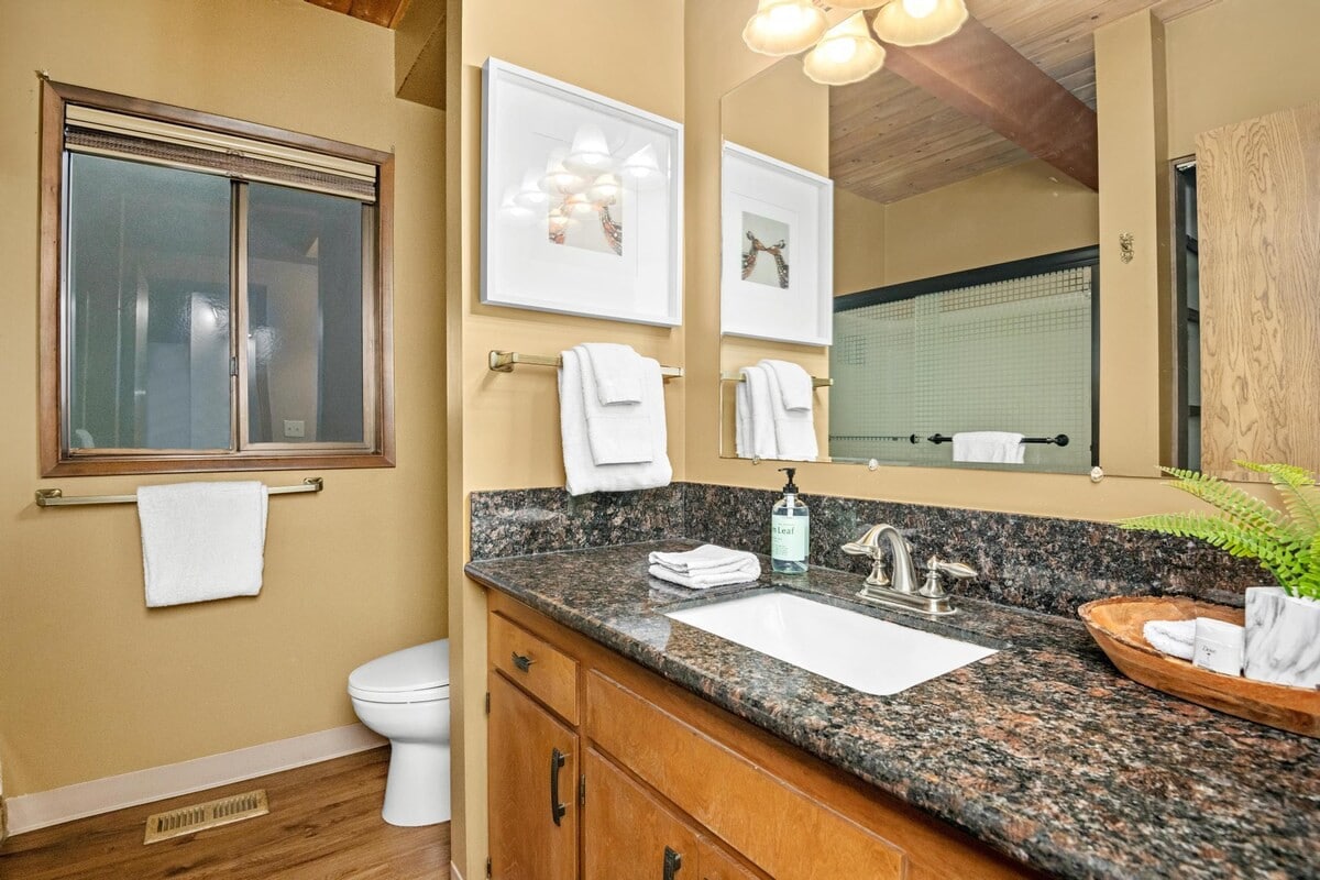 A closer view of the bathroom vanity, showcasing a speckled granite countertop, a white undermount sink with a brushed nickel faucet, and a large mirror. White framed art and fresh towels add a touch of comfort.