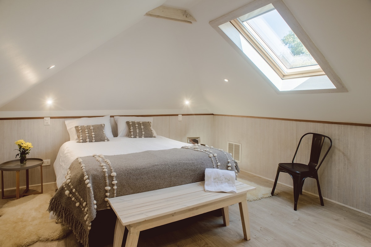 Relax in this charming attic bedroom with a skylight view, plush bedding, and cozy decor—your perfect retreat.