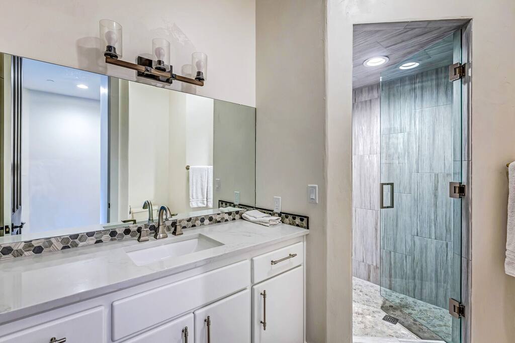 Clean bathroom w/ vanity, mirror, and glass-enclosed shower.