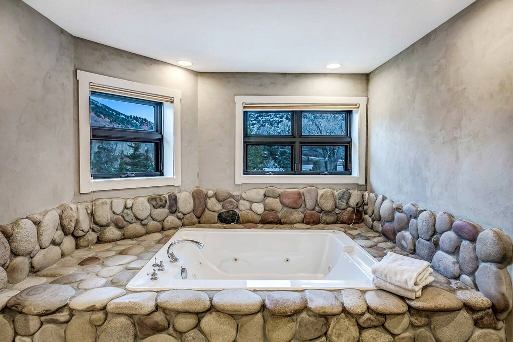 Deep soaking tub framed by natural stone & windows, perfect for long, relaxing baths at the end of the day.