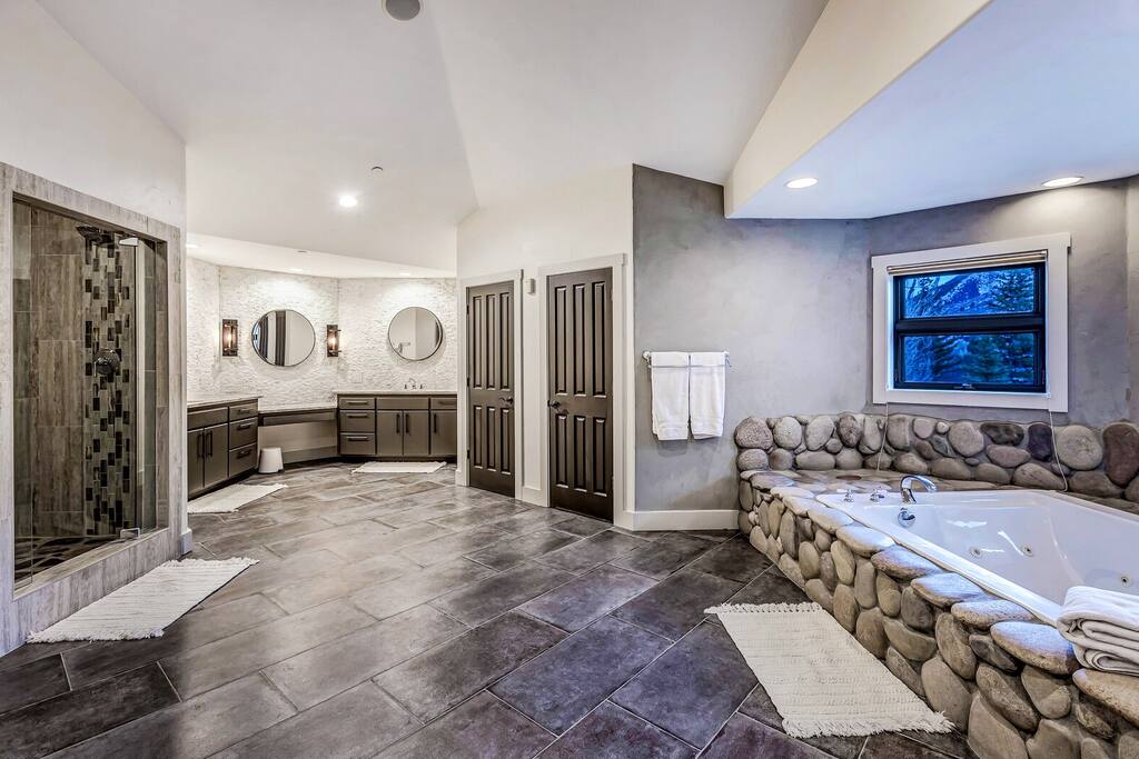 Spa-like bathroom w/ stone floors, expansive vanity & warm lighting, creating a calm space to refresh and unwind.