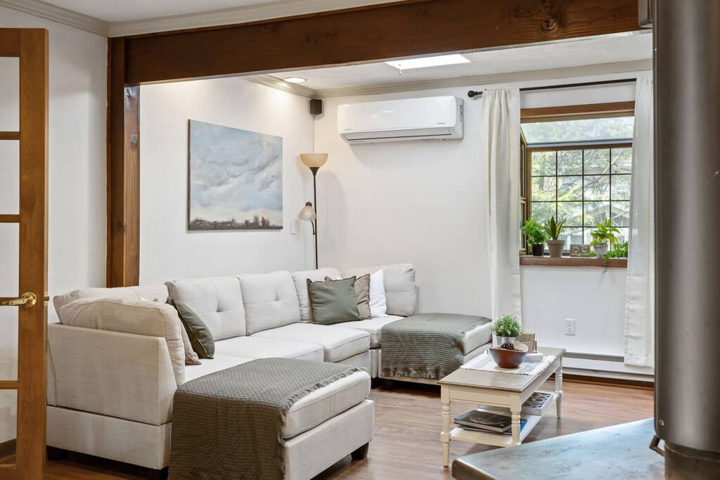 A bright and inviting corner featuring a cushy sectional, wood beams, and window views that bring in the light and nature.