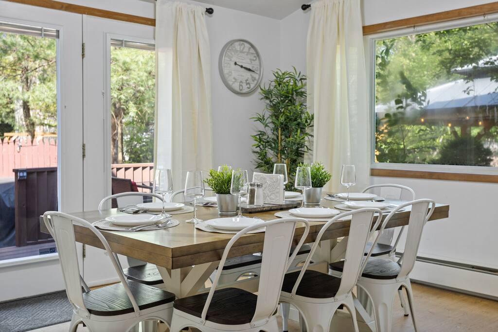 Window-Wrapped Dining Setup
A spacious table framed by large windows and soft curtains makes this room feel open, bright, and perfect for shared meals.